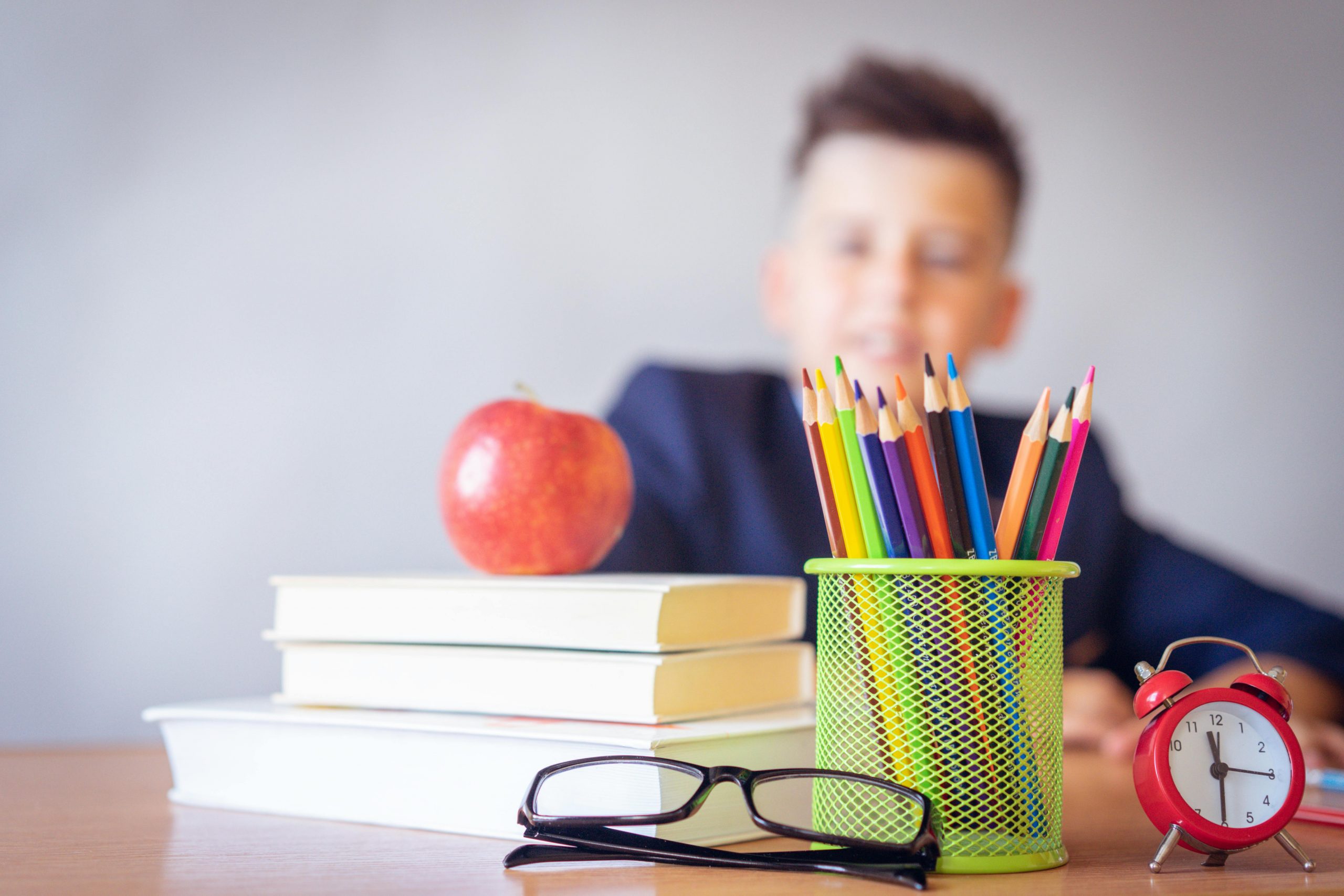 Services Schoolboy smiling behind a desk with books, pencils, and an alarm clock symbolizing study and creativity.